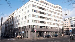 Un edificio de varios pisos con un diseño arquitectónico moderno, que presenta una entrada a nivel de calle y varios balcones.