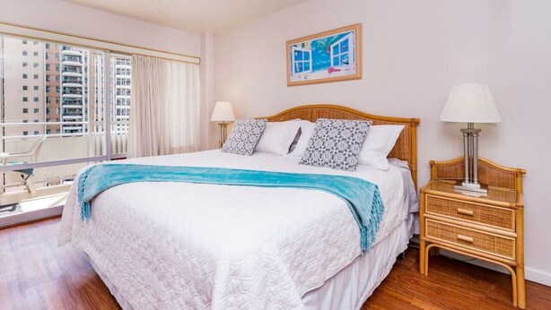 A bedroom with a large bed, a nightstand, a window with curtains, and a painting on the wall. - 1438 · Ilikai collection # 8. Beach Views and great value (Honolulu)