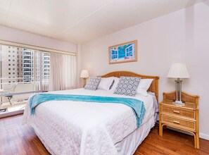 A bedroom with a large bed, a nightstand, a window with curtains, and a painting on the wall.