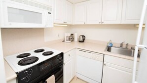 A compact kitchen with white cabinets, a stove, a microwave, a dishwasher, and a sink. - 1438 · Ilikai collection # 8. Beach Views and great value (Honolulu)