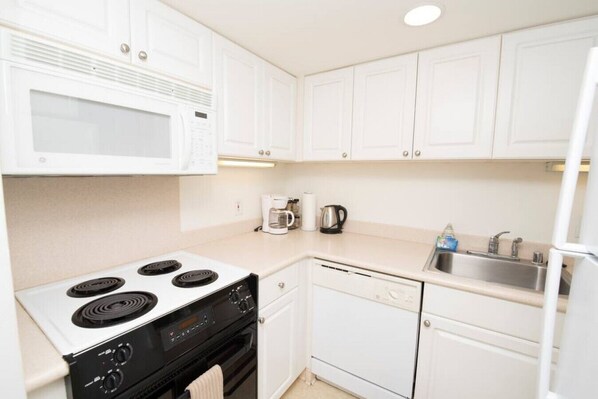 A compact kitchen with white cabinets, a stove, a microwave, a dishwasher, and a sink.