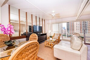 A modern living room with a sofa, chairs, a TV, and a balcony with a view of buildings.