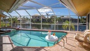 An indoor swimming pool with a swan float, a covered patio, and a view of a body of water and buildings. -  Waterfront House | Private Heated Pool &. Jacuzzi| 1 mile to beach| 5 Beds (Marco Island)