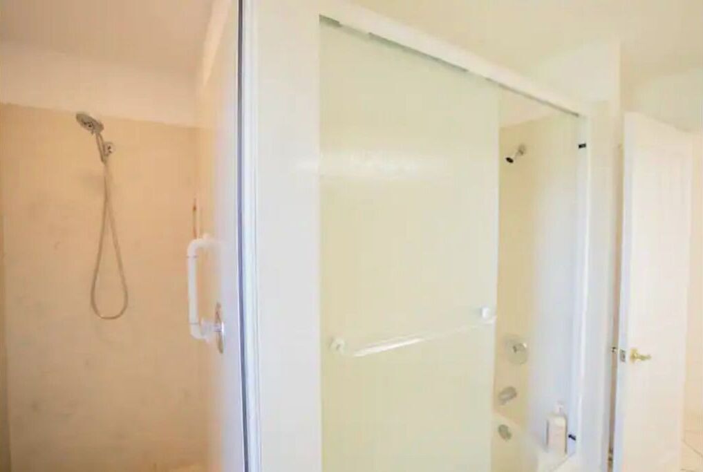 A bathroom with a glass shower enclosure, a visible showerhead, and a door with a handle.