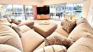 A spacious living room with a large sofa set, a flat-screen TV, and a view of a pool and outdoor area through large windows. -  Waterfront House | Private Heated Pool &. Jacuzzi| 1 mile to beach| 5 Beds (Marco Island)