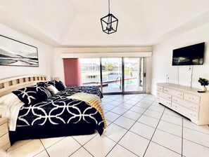 Une chambre avec un lit, une télévision, une porte-fenêtre coulissante donnant sur une zone avec piscine et un luminaire au plafond.
