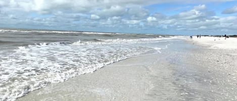 A beach with waves gently lapping onto the shore, a clear sky, and a few people in the distance.