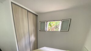 Une chambre à coucher comprenant un lit, une table de chevet, une fenêtre donnant sur un espace verdoyant et une porte coulissante.