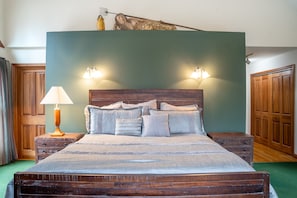 A bedroom with a wooden bed, two bedside tables, a lamp, and a green wall.