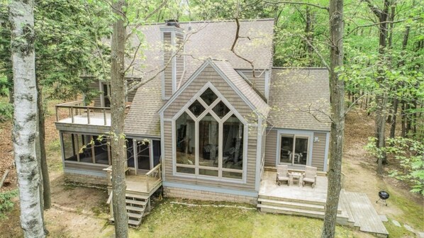 A cabin with a large front window, a deck, and a chimney.