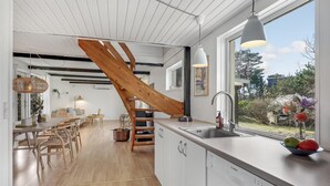 Una cocina moderna con un ventanal grande, una escalera de madera y un comedor con mobiliario de madera.