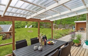 A covered patio with a table set for dining, surrounded by chairs, and a view of the backyard.