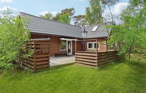 A wooden cabin with a tiled roof, a porch, and a small deck.