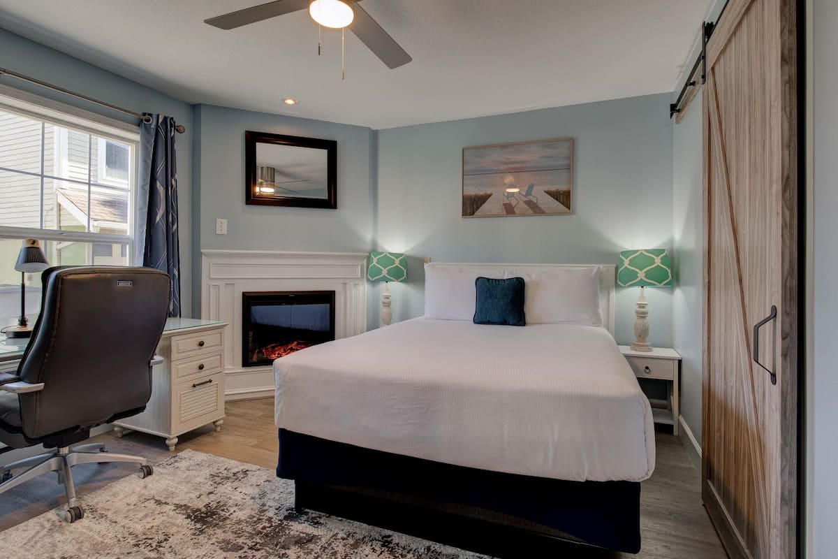 A bedroom with a large bed, a desk, a chair, a fireplace, and a wardrobe.