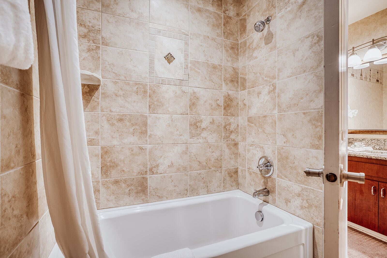 A bathroom with a white bathtub, beige tiles, and a wooden cabinet in the background.