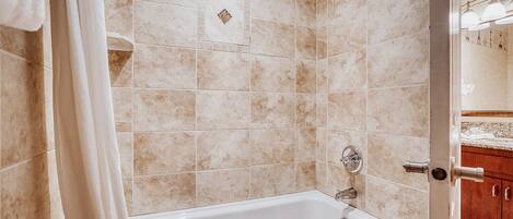 A bathroom with a white bathtub, beige tiles, and a wooden cabinet in the background.
