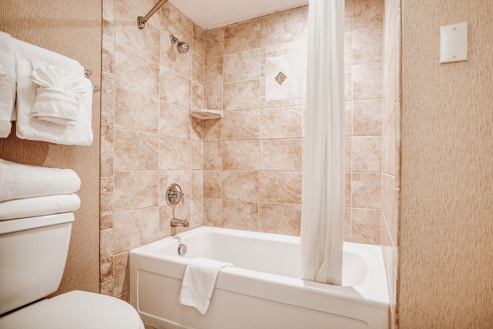 A bathroom with a bathtub, a shower, and a toilet. There are towels hanging on the wall.