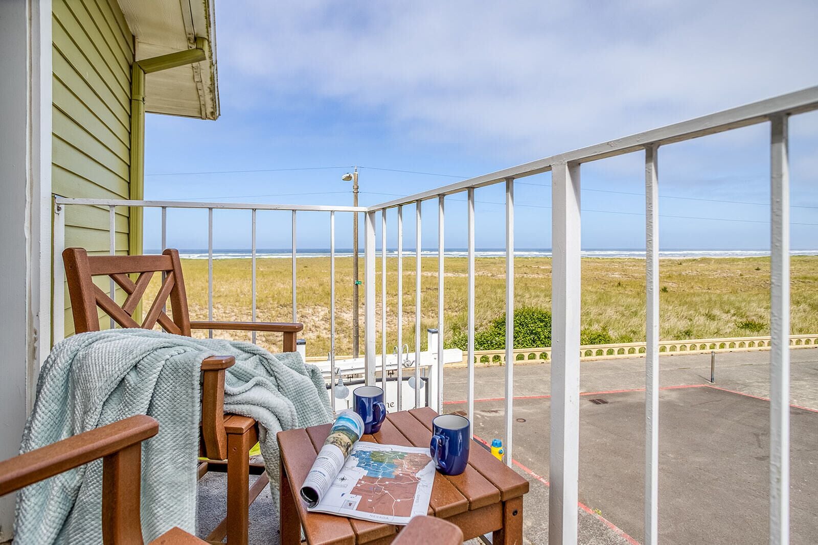 A wooden chair and table on a balcony with a view of the beach and ocean.