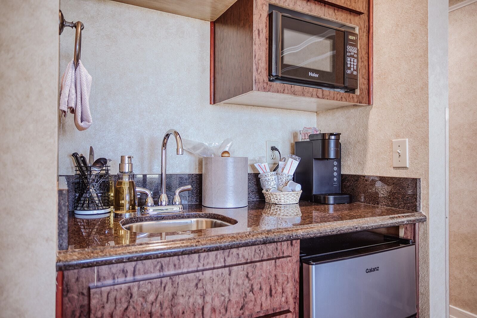 A modern kitchen with a granite countertop, stainless steel sink, and a built-in microwave.