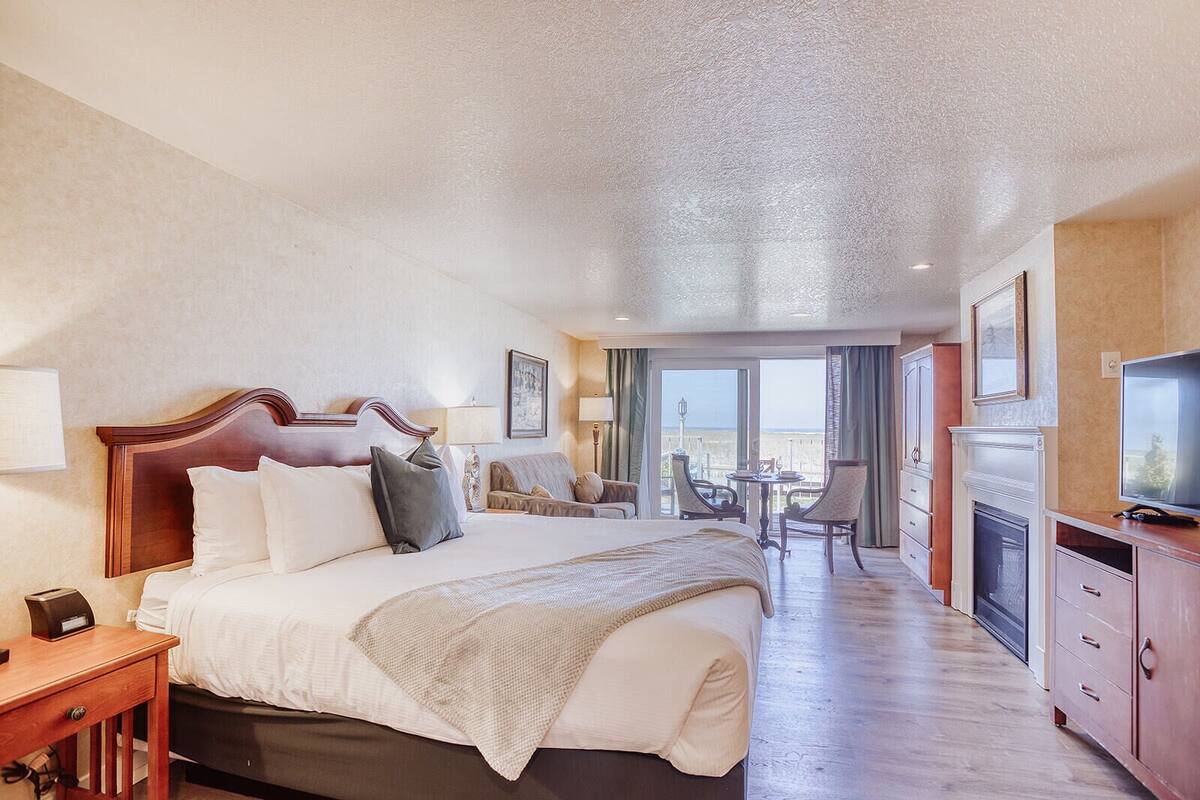 A hotel room with a large bed, a desk, a television, and a balcony with a view.