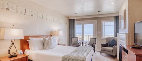 A hotel room with a large bed, a desk with a lamp, a TV, a chair, a balcony with a view, and a wall with a decorative pattern.