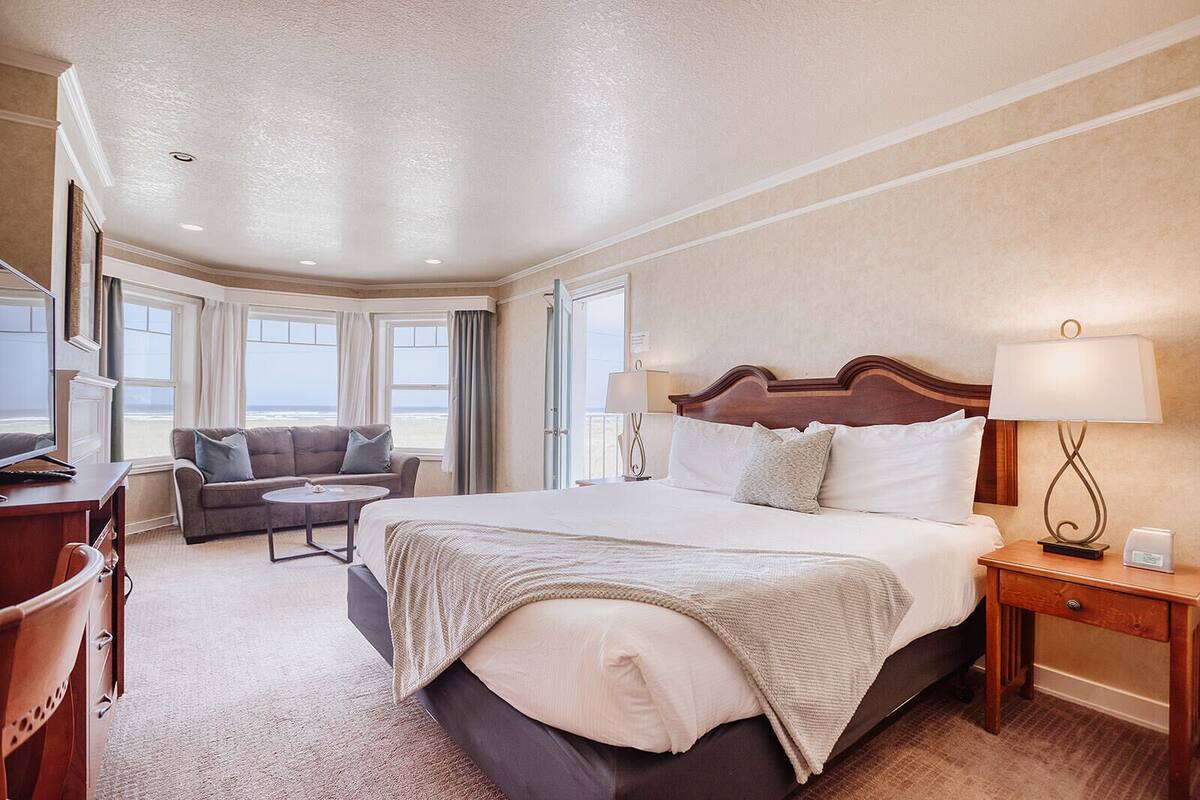 A hotel room with a large bed, a sofa, a desk, and a view of the beach.