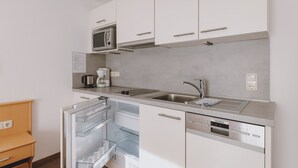 Een kleine keuken met witte kastjes, een ingebouwde magnetron, een koffiezetapparaat en een vaatwasser.