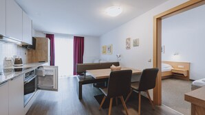 Habitación de hotel compacta con kitchenette, zona de comedor con banco, una cama individual y una mesita de noche pequeña.
