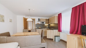 A modern kitchen with wooden cabinets, a dining area with a bench, and a TV on a wooden stand. - Appartements Sulzer - TOP 11 (Zell am See)
