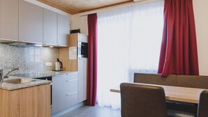 Et moderne køkken med træskabe, en granitbordplade og en indbygget ovn. Der er et spiseområde med et træbord og stole.