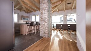 A modern kitchen with a stone column, wooden ceiling beams, and a dining area with chairs and a table. - Appartements Sulzer - TOP 31 (Zell am See)