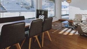 A modern living room with a sofa, chairs, a coffee table, and a view through large windows. - Appartements Sulzer - TOP 31 (Zell am See)