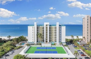 Un hôtel doté d’un court de tennis, offrant une vue sur la plage et comprenant plusieurs immeubles de grande hauteur.