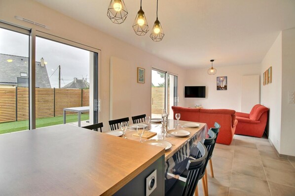 A modern kitchen with a wooden countertop, a dining area with chairs and a table set for four, and a red sofa in the background.