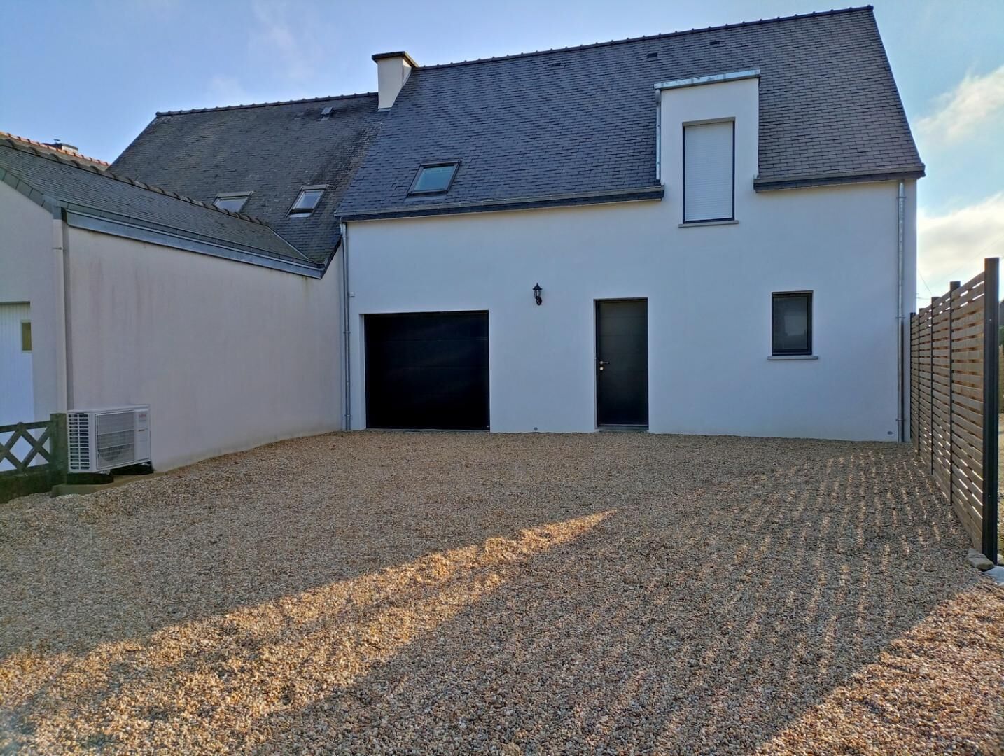 Ein modernes, zweigeschossiges Haus mit Kiesweg, Garage und umzäunter Hinterhof.