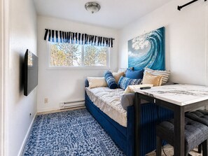 Een slaapkamer met een bed, een tafel, een televisie, een raam met gordijnen en een schilderij.