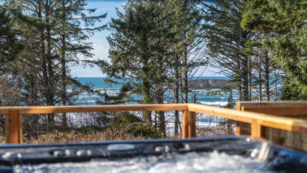 Ein Whirlpool mit einer Holzterrasse mit Blick auf eine Küstenlandschaft mit Bäumen und Klippen.