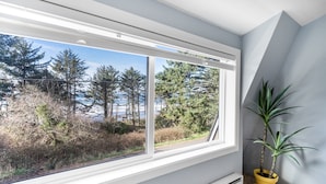Ein Zimmer mit großem Fenster und Blick auf Bäume und eine Straße. Ein Topfpflanze steht auf dem Fensterbrett.