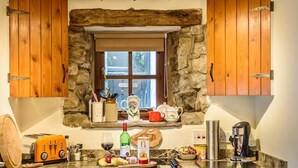 A kitchen with stone walls, wooden cabinets, a window, and various kitchen items.