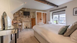 A bedroom with a stone fireplace, a bed with pillows, a TV mounted on the wall, and a window with a view.