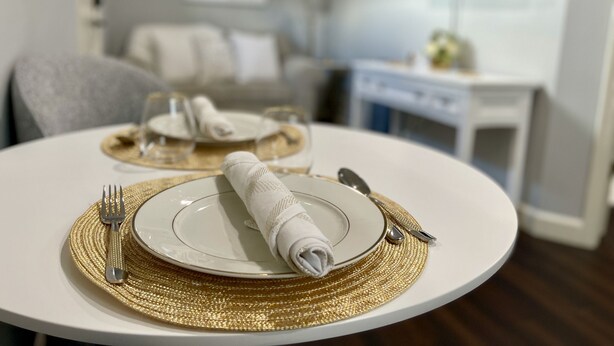 Une table à manger dressée avec de l’assiette blanche, des sets de table dorés et des couverts en argent.