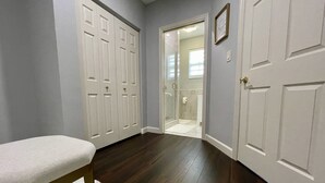 Un couloir avec un banc, une porte donnant sur une salle de bain et un placard avec plusieurs portes.