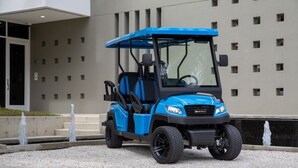 Une voiturette de golf bleue est garée devant un bâtiment à la façade moderne, ornée d’une série de fenêtres carrées.