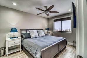 Une chambre à coucher avec un lit, deux tables de chevet avec des lampes, un ventilateur de plafond, une fenêtre avec vue et une petite poubelle.