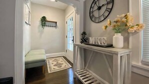A hallway with a white bench, a decorative clock, and a vase with flowers on a console table. - Sunny 3BR Craftsman Bungalow | Bay View (Milwaukee)