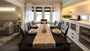 A dining room with a long table set for six, flanked by a sofa and a kitchen area with cabinets and a countertop. - Sunny 3BR Craftsman Bungalow | Bay View (Milwaukee)