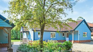 Une maison bleue avec un toit en tuiles, entourée d’un jardin où poussent différentes plantes et fleurs.