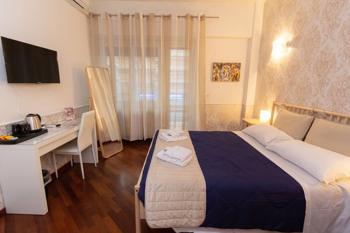 Ein Hotelzimmer mit Bett, Schreibtisch, Stuhl, Fernseher und Duschvorhang.