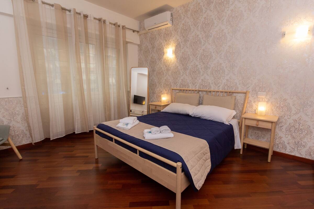 Ein Schlafzimmer mit einem hölzernen Bett, einem Nachttisch, einem Sessel und einem Spiegel.