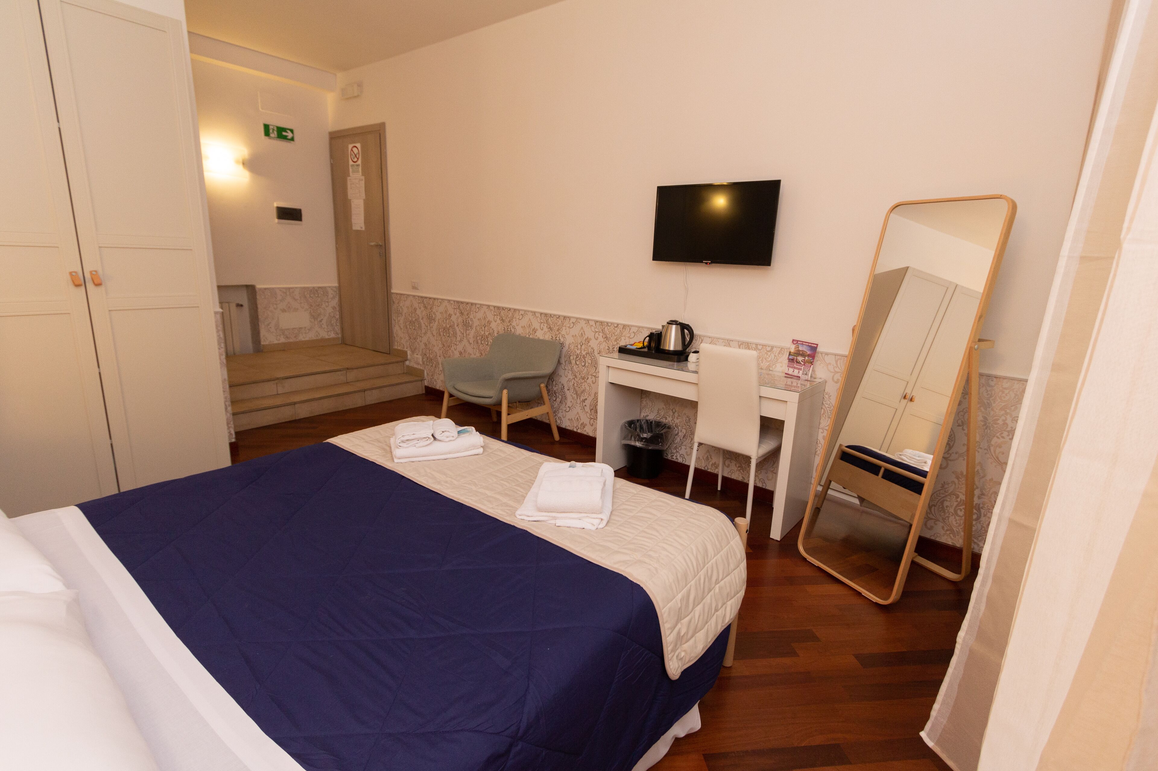 A hotel room with a bed, a desk, a chair, a TV, and a mirror.